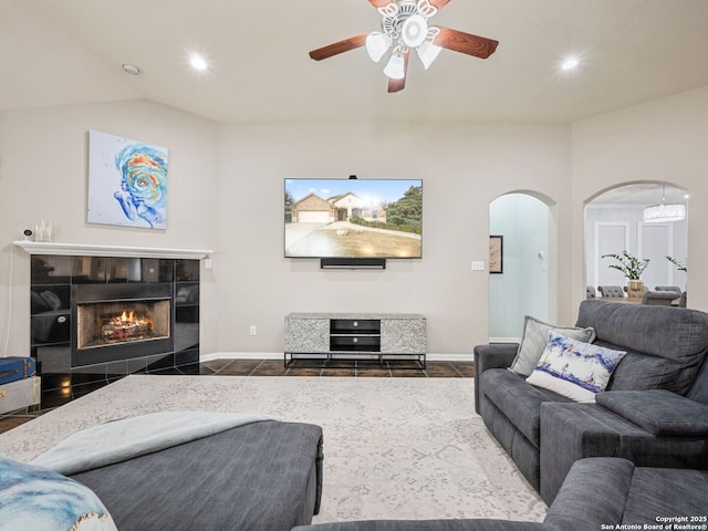 living room with ceiling fan, vaulted ceiling, and a tiled fireplace