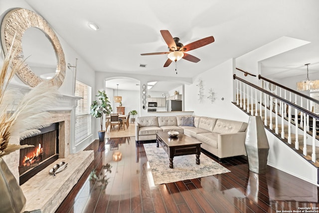 living room featuring ceiling fan with notable chandelier, a high end fireplace, and dark wood-type flooring