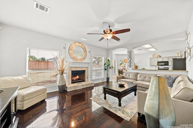 living room featuring a stone fireplace, dark wood-type flooring, and ceiling fan