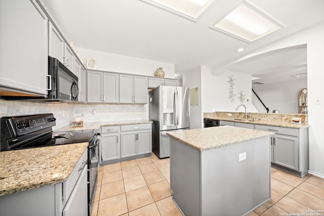 kitchen featuring light stone countertops, black appliances, decorative backsplash, a kitchen island, and sink