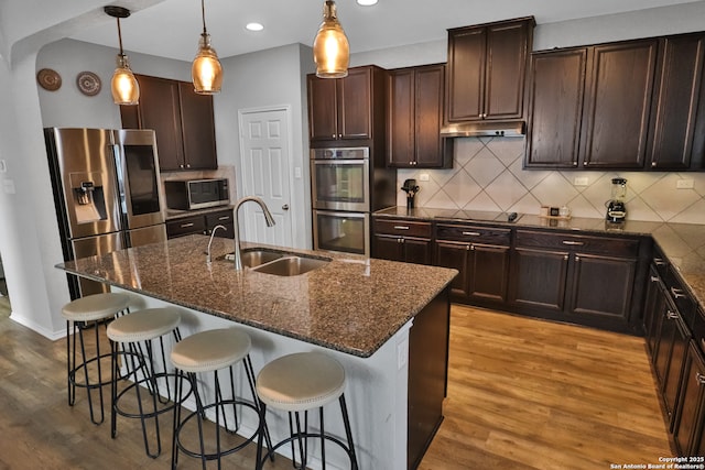 kitchen with stainless steel appliances, sink, a kitchen island with sink, and decorative light fixtures