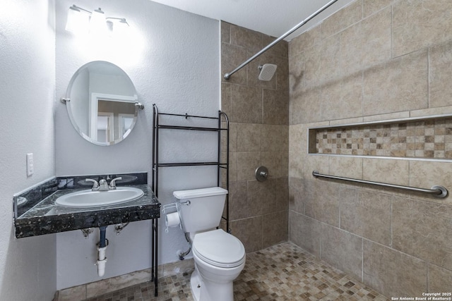 bathroom featuring sink, a tile shower, and toilet