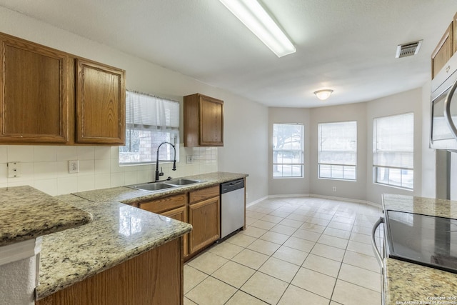 kitchen with appliances with stainless steel finishes, light stone countertops, decorative backsplash, light tile patterned floors, and sink