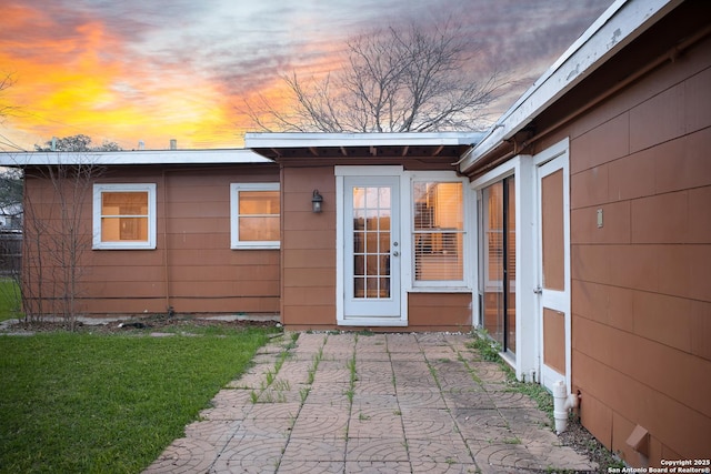 exterior entry at dusk with a patio area and a yard