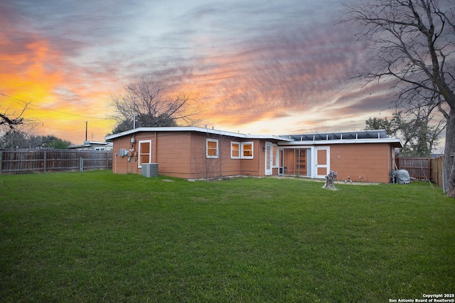 back house at dusk featuring a lawn and central air condition unit