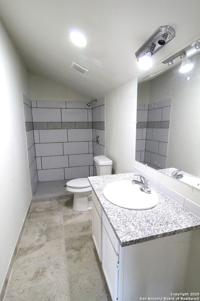 bathroom featuring tiled shower, vaulted ceiling, vanity, and toilet