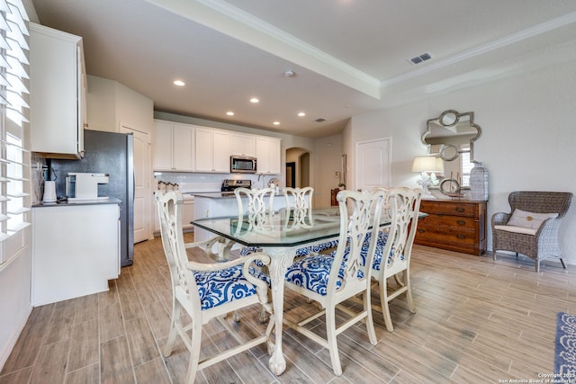 dining room with arched walkways, a raised ceiling, visible vents, and wood finish floors