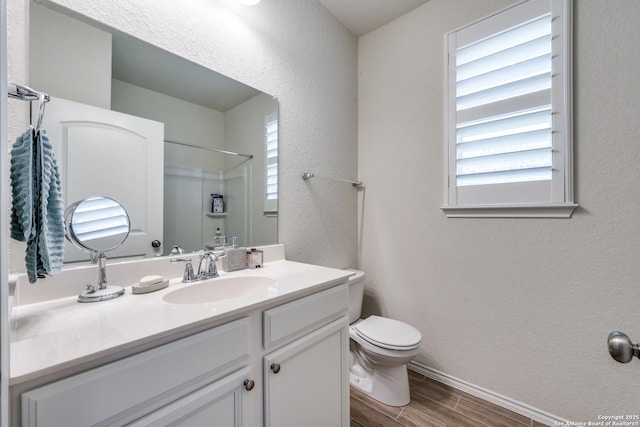 bathroom featuring a textured wall, toilet, wood finish floors, vanity, and a shower