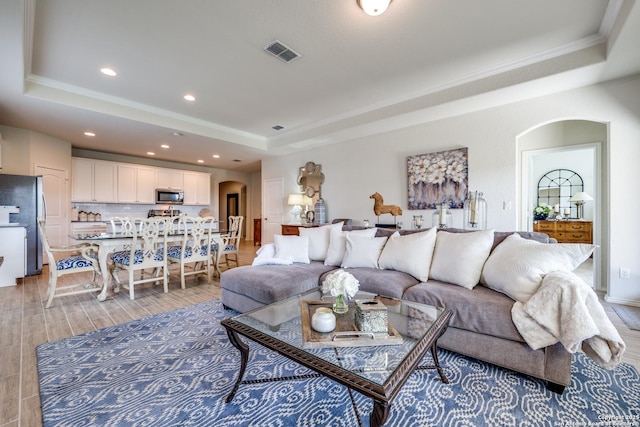 living room featuring arched walkways, a tray ceiling, light wood finished floors, and visible vents