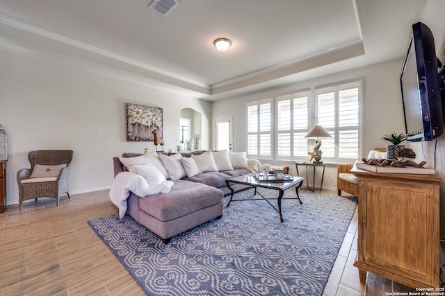 living room featuring light wood-type flooring, a raised ceiling, visible vents, and arched walkways