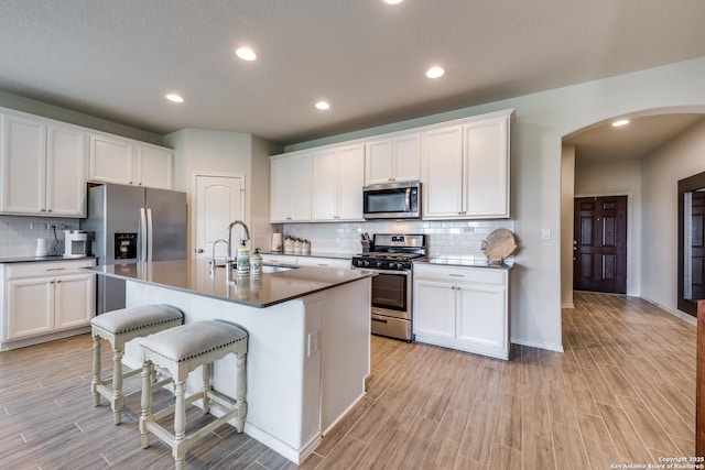 kitchen with appliances with stainless steel finishes, arched walkways, wood finish floors, and a sink