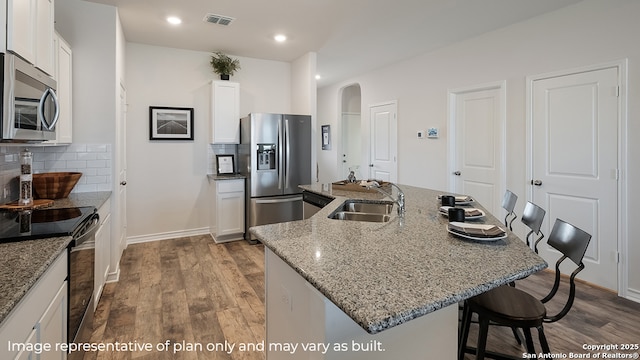 kitchen with appliances with stainless steel finishes, sink, light stone counters, white cabinets, and a kitchen island with sink