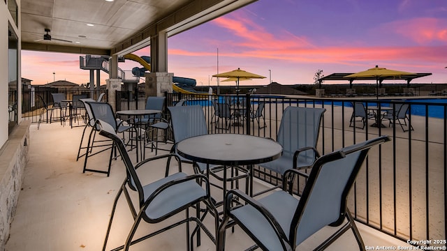 balcony at dusk featuring a patio, ceiling fan, and a community pool