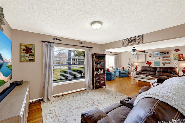 living room featuring light wood-type flooring, ceiling fan, and a textured ceiling