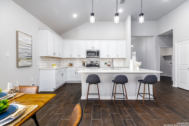 kitchen with wood finish floors, a breakfast bar, stainless steel appliances, light countertops, and a sink