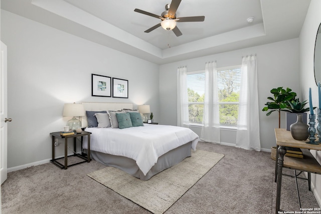 carpeted bedroom featuring a raised ceiling, a ceiling fan, and baseboards