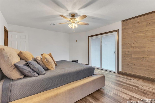 bedroom with light wood-type flooring, ceiling fan, and wood walls