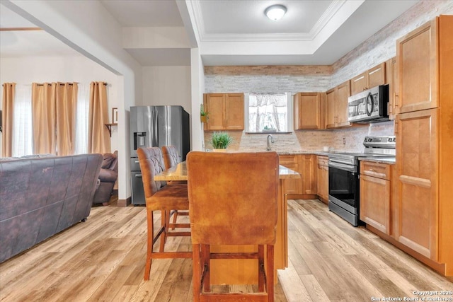 kitchen with stainless steel appliances, light hardwood / wood-style floors, a breakfast bar, a tray ceiling, and ornamental molding