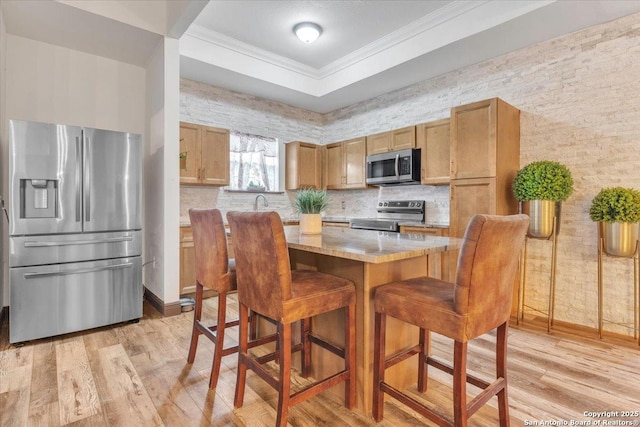 kitchen with light wood-type flooring, stainless steel appliances, crown molding, and a breakfast bar