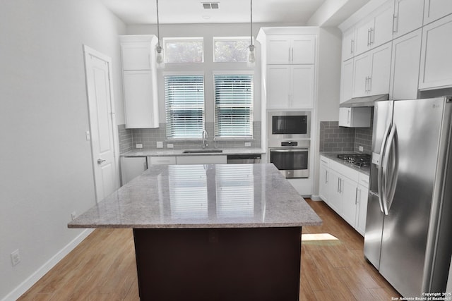 kitchen with backsplash, under cabinet range hood, light wood-style floors, appliances with stainless steel finishes, and a sink