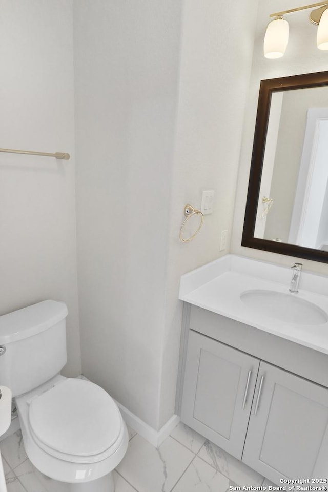 half bathroom featuring vanity, marble finish floor, baseboards, and toilet