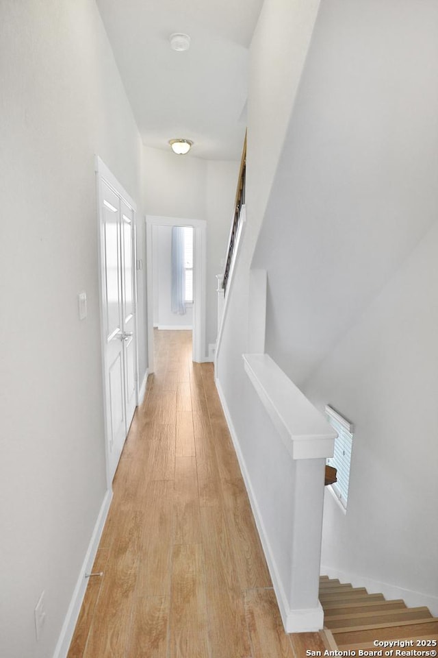 hallway featuring light wood-style flooring, baseboards, and stairway