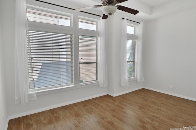 empty room featuring wood finished floors, ceiling fan, baseboards, and a wealth of natural light