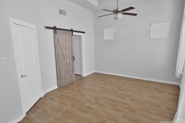 unfurnished bedroom with visible vents, baseboards, light wood finished floors, and a barn door