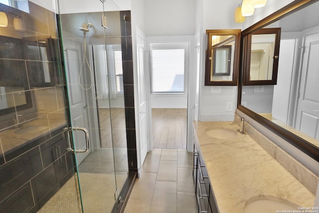 full bathroom featuring a stall shower, double vanity, a sink, and tile patterned floors