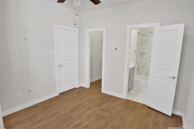 unfurnished bedroom with ensuite bathroom, light wood-style flooring, a ceiling fan, a walk in closet, and baseboards