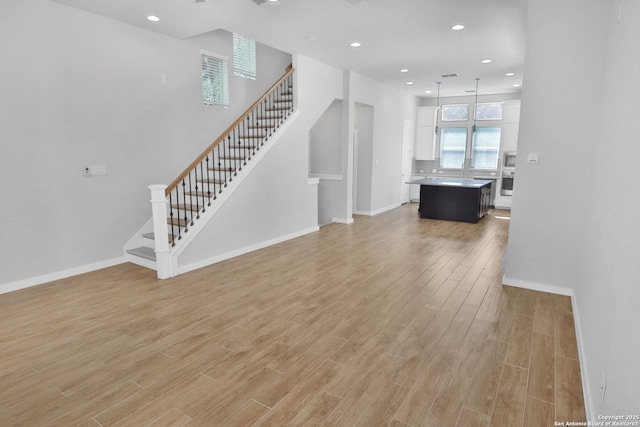unfurnished living room with baseboards, light wood-style floors, and stairs