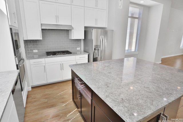 kitchen with light wood-style flooring, a kitchen island, white cabinets, under cabinet range hood, and stainless steel appliances