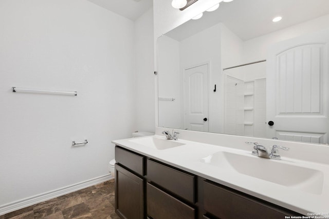 full bath featuring toilet, a sink, baseboards, and double vanity