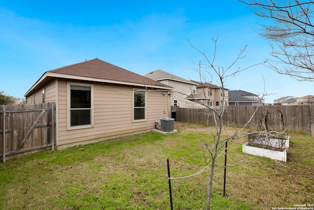 rear view of property featuring roof with shingles, a yard, a vegetable garden, central AC, and a fenced backyard