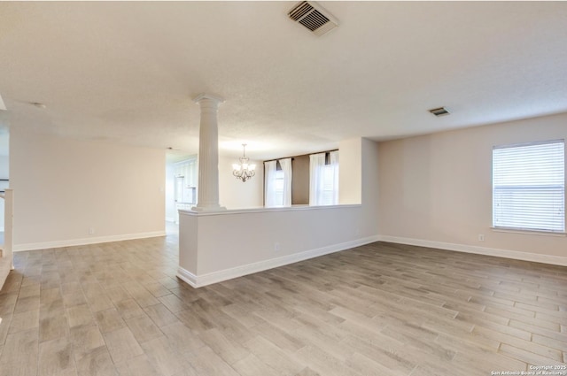 spare room with a notable chandelier, plenty of natural light, light hardwood / wood-style floors, and decorative columns