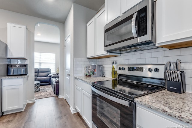 kitchen with arched walkways, appliances with stainless steel finishes, wood finished floors, and white cabinets