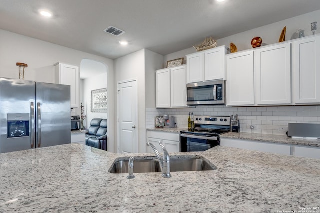 kitchen featuring arched walkways, stainless steel appliances, a sink, visible vents, and decorative backsplash