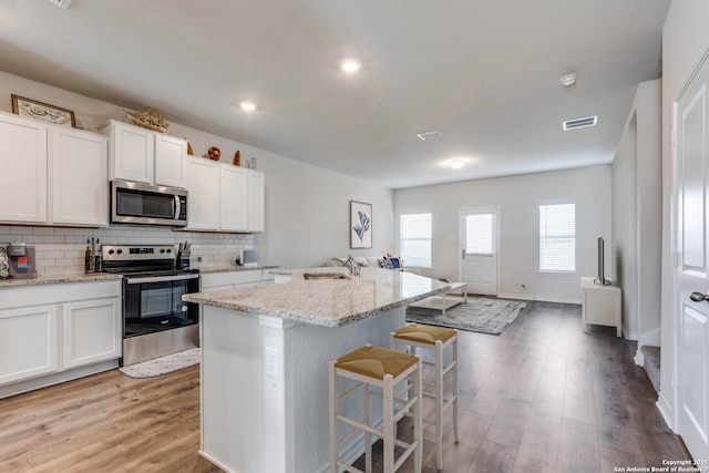 kitchen featuring a breakfast bar, stainless steel appliances, tasteful backsplash, a sink, and light wood-type flooring