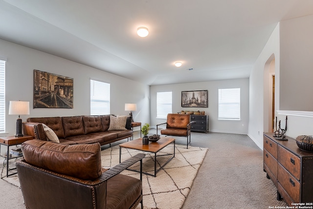 living room featuring arched walkways, light colored carpet, and baseboards