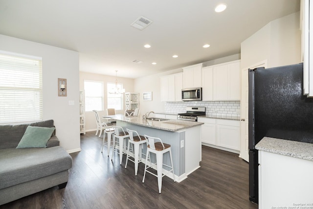 kitchen featuring appliances with stainless steel finishes, a center island with sink, white cabinets, pendant lighting, and a breakfast bar