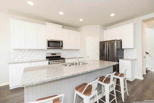 kitchen with appliances with stainless steel finishes, an island with sink, light stone countertops, white cabinets, and sink