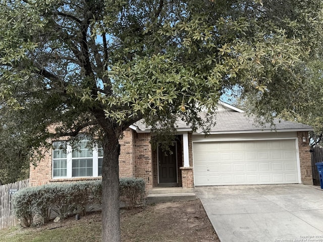 view of property hidden behind natural elements featuring a garage, concrete driveway, brick siding, and fence