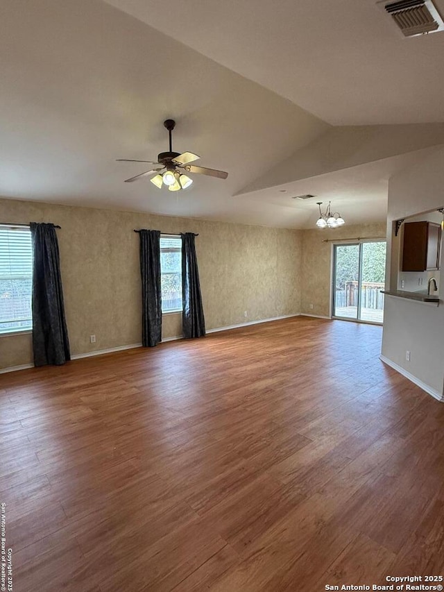 unfurnished living room with ceiling fan with notable chandelier, wood-type flooring, and a wealth of natural light