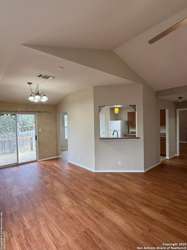 unfurnished living room featuring an inviting chandelier, vaulted ceiling, and wood-type flooring