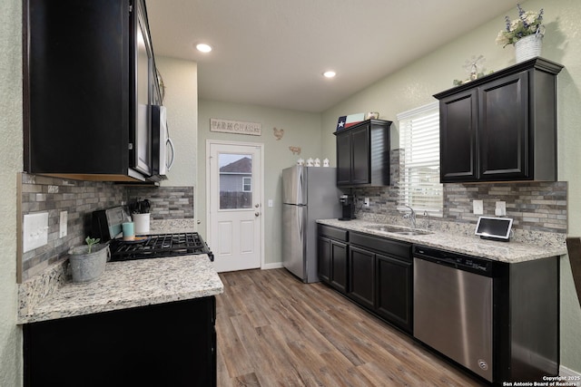 kitchen featuring stainless steel appliances, light stone counters, decorative backsplash, light hardwood / wood-style floors, and sink