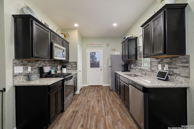 kitchen featuring tasteful backsplash, wood-type flooring, stainless steel appliances, light stone countertops, and sink