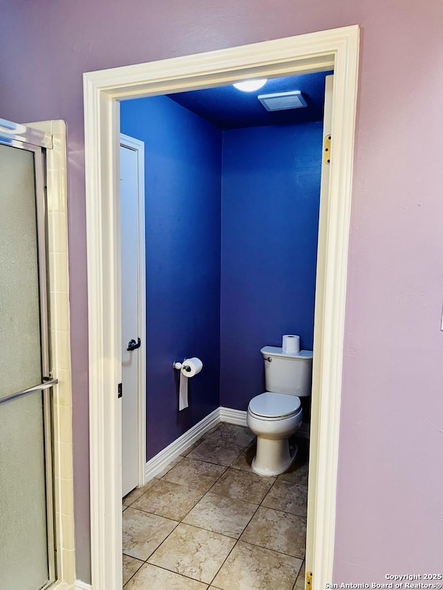 bathroom featuring tile patterned flooring, toilet, and a shower with shower door