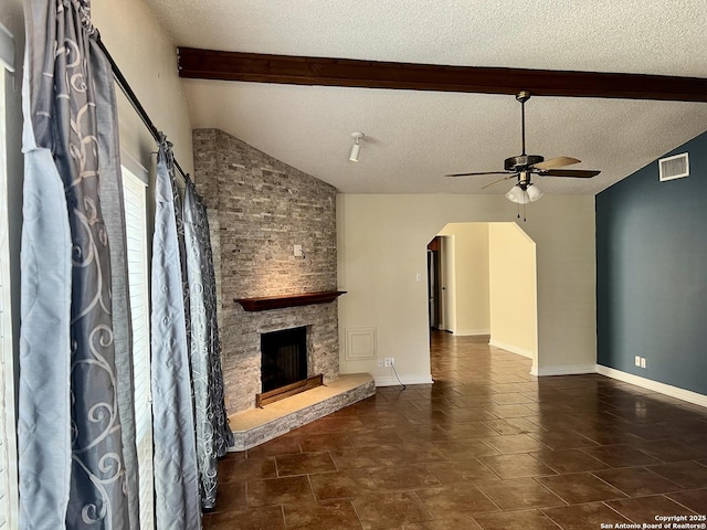 unfurnished living room with ceiling fan, a stone fireplace, vaulted ceiling with beams, and a textured ceiling