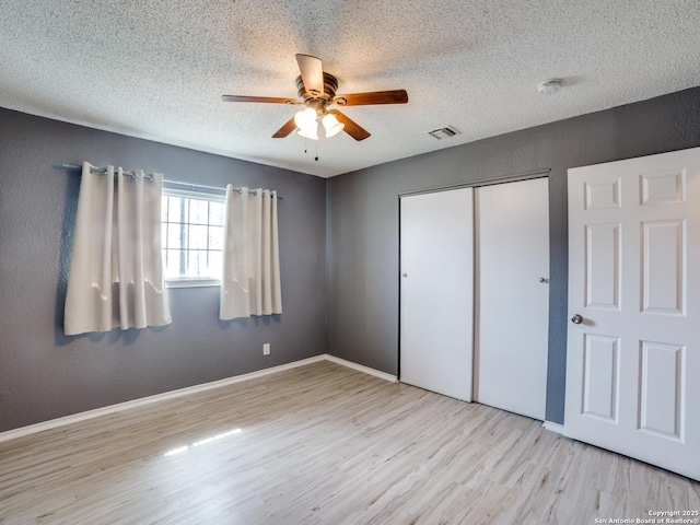 unfurnished bedroom with ceiling fan, light hardwood / wood-style floors, a textured ceiling, and a closet