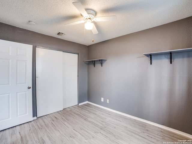 unfurnished bedroom featuring ceiling fan, light wood-type flooring, a textured ceiling, and a closet